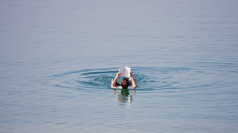 En person flyter p rygg i Dda havet och lser en bok.